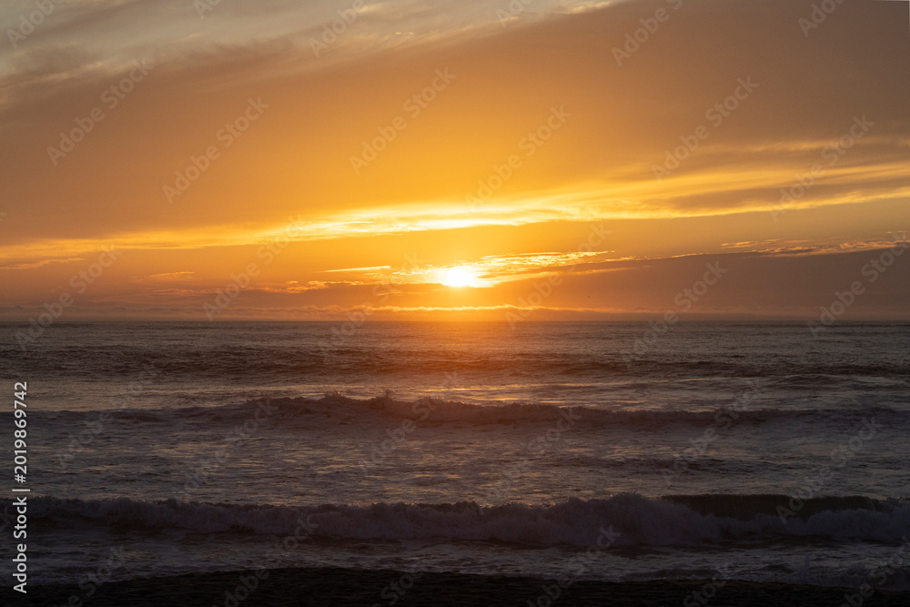 Obraz premium Golden sunset over the ocean with gentle waves and dramatic clouds