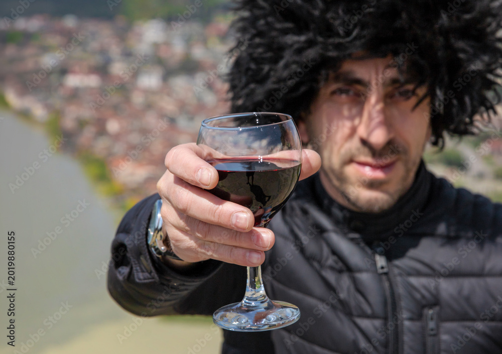 Fototapeta premium Georgian man in a papakhi with a glass of wine. Selective focus.
