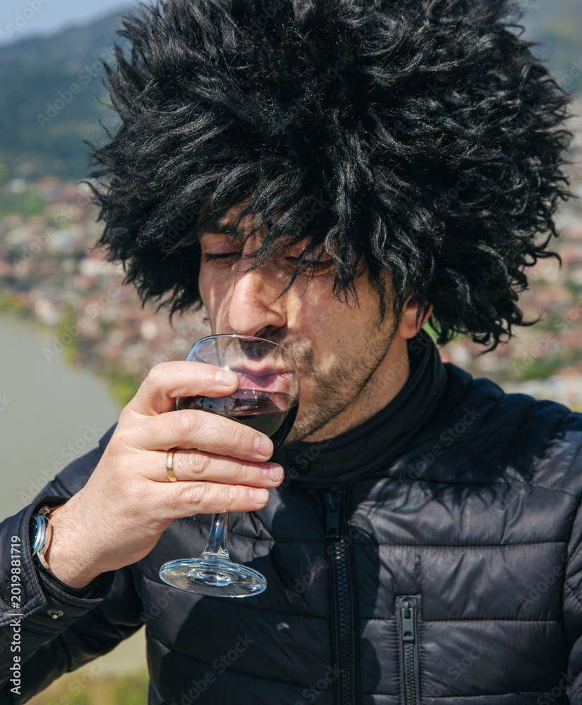 Fototapeta premium Georgian man in a papakhi with a glass of wine. Selective focus.