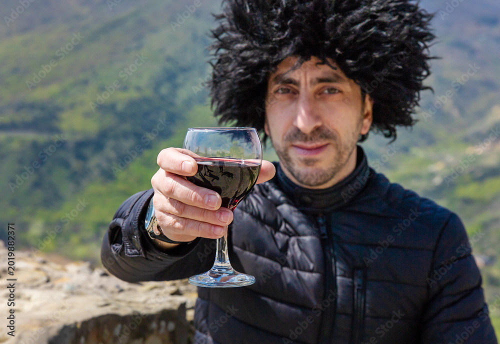 Fototapeta premium Georgian man in a papakhi with a glass of wine. Selective focus.