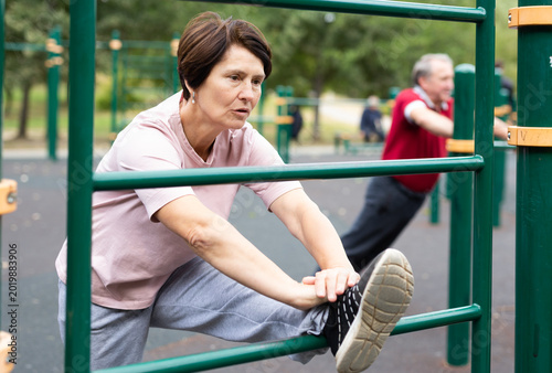 Obraz na plátně elderly woman stretches on the bars in an outdoor sports area