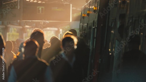Commuters board train at station during morning light in city