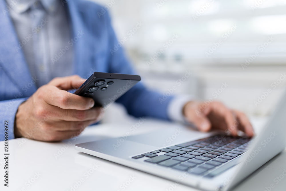 Fototapeta premium Businessman Using Smartphone Beside Laptop in Office