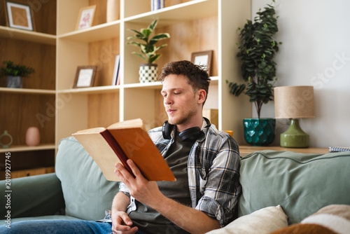 Foto Young man reading book on sofa at home