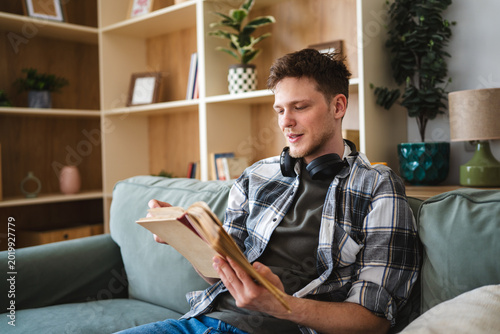 Konstfotografi Young man reading book on sofa at home