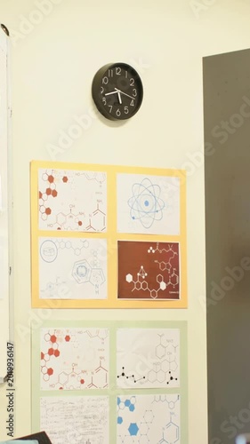 Vertical video: Panning camera shifting downward to reveal lab wall with black clock and posters