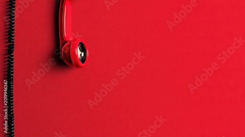 Red vintage telephone handset hanging against a vibrant red wall with a black coiled cord in a minimalist macro shot for communication marketing