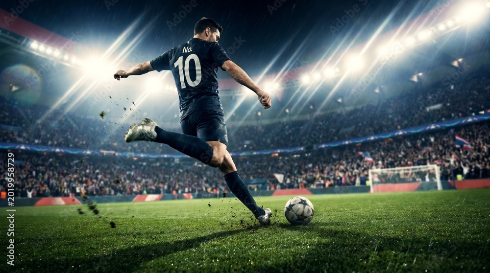 Naklejka premium A professional football player in black jersey kicking ball on a stadium field during a night match.