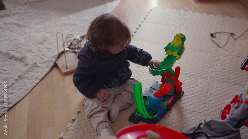 фотографія Toddler sitting on padded floor mat playing with colorful plastic toy track in c