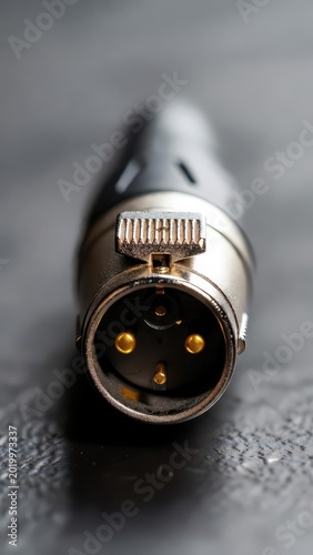 Extreme close-up of a silver XLR connector with gold pins on a dark textured surface