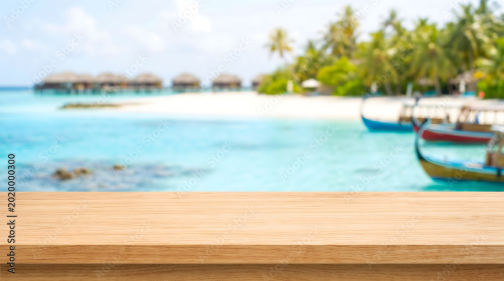 Fototapeta premium Empty wooden tabletop for product display with blurred tropical beach background for summer marketing design.