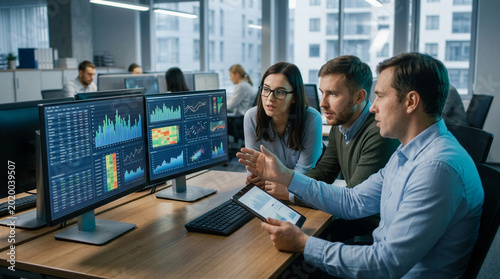 Data analysts monitoring complex financial information on multiple computer screens in a tech office.