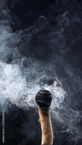 Close up of an extinguished torch with heavy swirling smoke on a dark background. Concept of burnout, end of fire, aftermath, danger, and atmospheric element for design use.