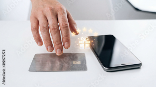 A hand holding a credit card near a smartphone with a gift icon, symbolizing online shopping and digital transactions.