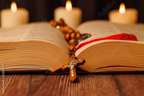 Olive wood rosary on an open bible with purple cover and white candles for illustrating christianity and spiritual devotion today.
