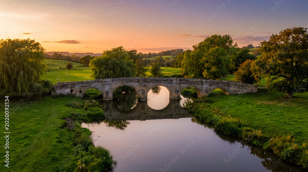 Fototapeta premium Old stone arch bridge reflection in river at sunset