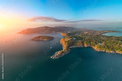 An expansive aerial view reveals the stunning Phuket coastline nai harn beach Promthep Cape, with a wide sandy beach curving into a bay dotted with numerous boats