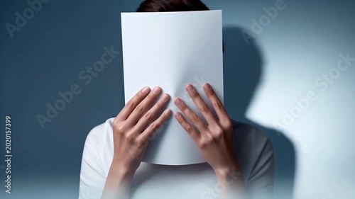 A woman hiding her face behind a blank sheet of white paper.