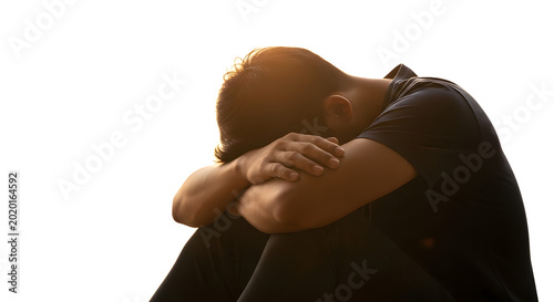 A man sits in a contemplative pose with his head in his hands against a bright background