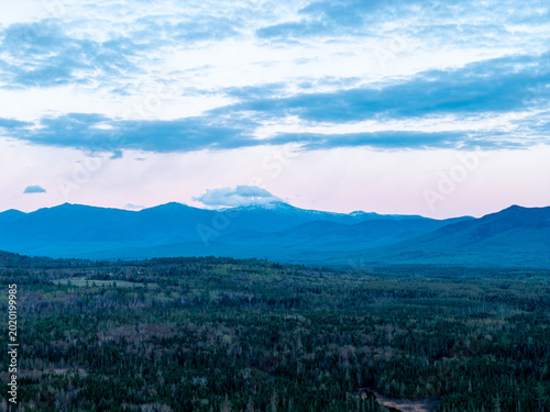Foto White Mountains northern New Hampshire landscape, aerial drone view over vast pine forests looking toward distant blue mountain peaks with snow-dusted summits under a twilight sky