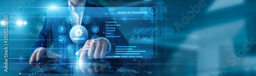 Photos Project Coordinator touching the tablet using Work In Progress, displayed diagrams and graphs with icons of ongoing tasks, development stages, workflow tracking across the world map