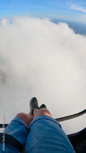 POV view of a man's legs and feet dangling over a thick layer of clouds during a paragliding flight in Rio de Janeiro, Brazil.