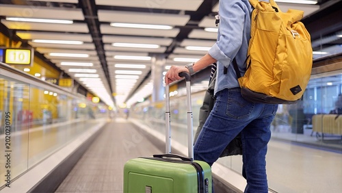 Fotografía Traveler with backpack and green luggage moving along a long airport walkway, re