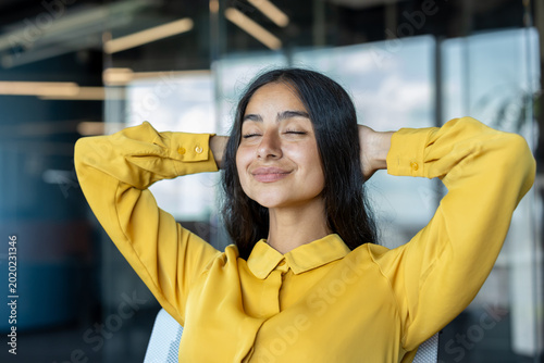 Photography Close-up photo of a young Indian woman sitting in an office chair, eyes closed,