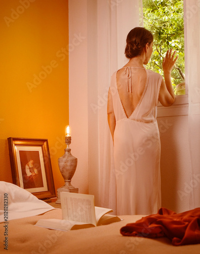 Scene of a woman in a romantic pose wearing a nightgown, looking out of her bedroom window