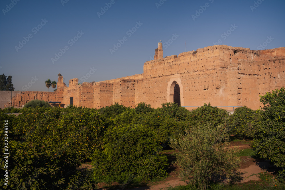 Fototapeta premium Historic walls of El Badi Palace in Marrakech during golden hour light. Iconic Moroccan architecture and ancient fortress surrounded by palm trees and gardens.