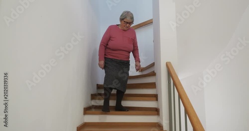 Elderly woman carefully walking down the wooden stairs using the handrail