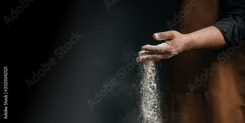 Baker hands dropping flour on dark background with copy space for artisan bakery advertising