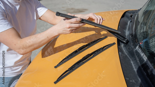 A woman replaces old windshield wipers with new ones on a car.