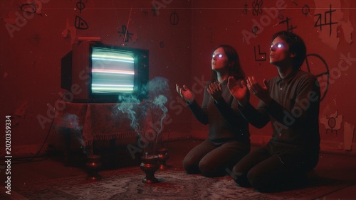 Woman and man with glowing eyes kneeling before television screen in dark room. Mind control and hypnosis concept. Psychological manipulation and zombie behavior in cult ritual atmosphere.