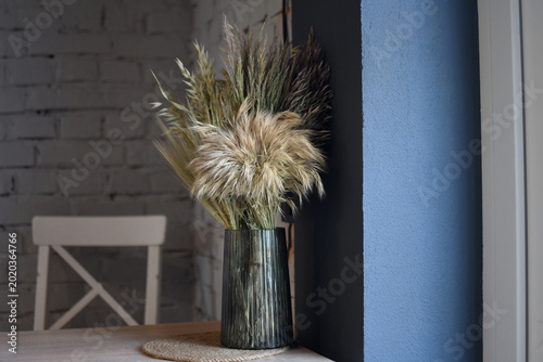 Elegant Dried Pampas Grass Bouquet in Dark Ribbed Glass Vase on Wooden Table Against Moody Brick Wall Interior. Selective focus.
