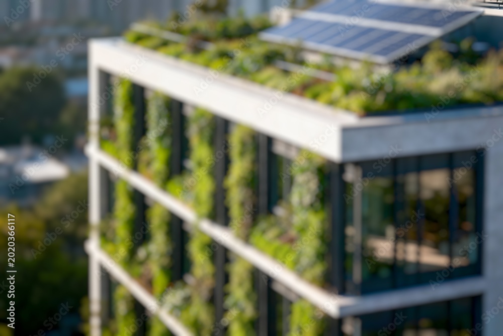 Fototapeta premium Defocused sustainable modern office building featuring green walls, rooftop plants, and renewable solar energy technology.