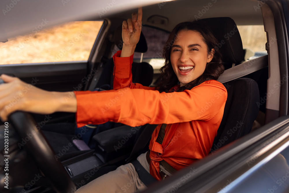 Naklejka premium Young woman inside car smiling and pointing upward with finger