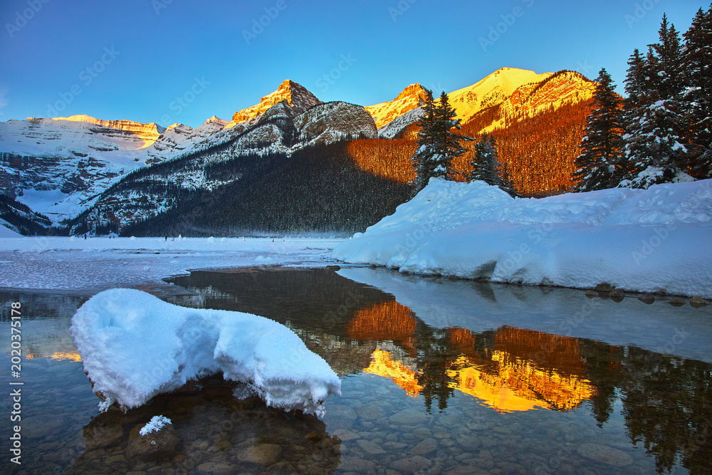 Obraz premium Snow Covered Mountains Sunrise Reflection on Frozen Lake with Evergreen Trees Winter