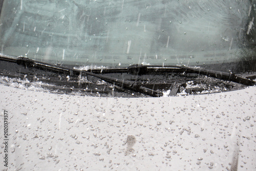 Hail stones falling on a silver car hood during a hailstorm