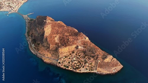 Aerial view of the massive rock of Monemvasia with its medieval town and stone houses surrounded by the deep blue Aegean Sea in Monemvasia, Greece.