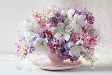 Spring bouquet of lilacs, hyacinths, bird cherry and apple blossoms in a cup on the table, beautiful card