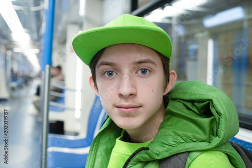  Portrait of a smiling teenage boy in green cap riding inside subway train car