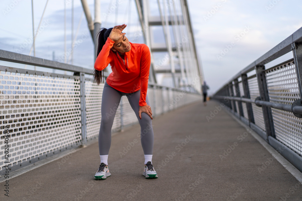Obraz premium Woman runner catching her breath on a bridge after a strenuous workout
