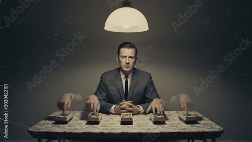 Man in suit operating multiple remote control devices on table. Concept of mind control, brainwashing and human subconscious influence. Surveillance technology and psychological manipulation.
