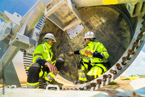 Принти на полотні Professional wind turbine technicians in safety gear performing a detailed technical inspection inside a turbine component at a renewable energy site
