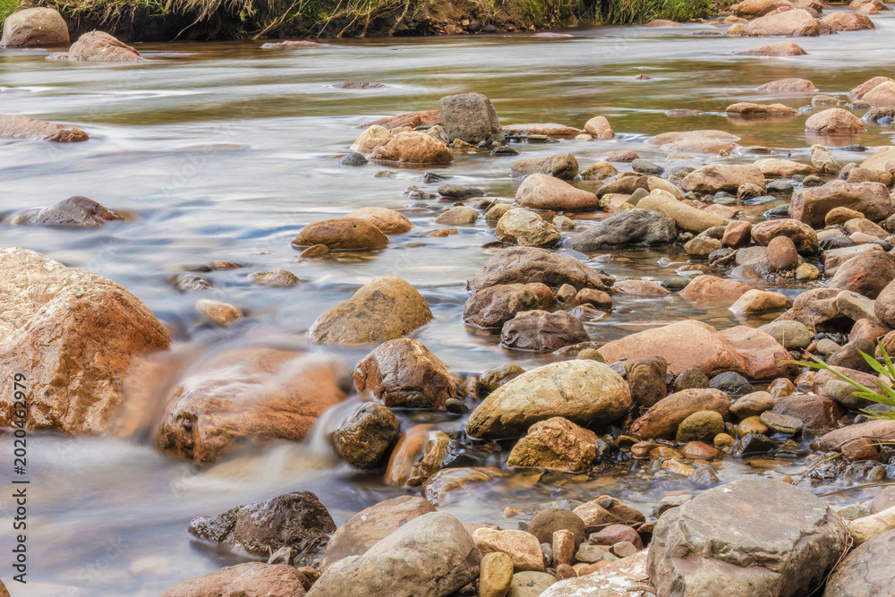Obraz premium The current of a river flowing over rocks and stones