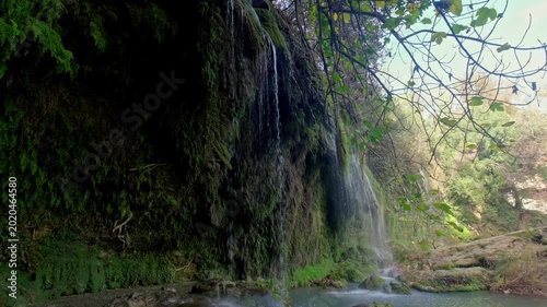 Close-up view of water flowing over mossy rocks in a lush forest, showing a peaceful waterfall scene with green vegetation, wet cliffs and natural daylight for travel and nature footage.