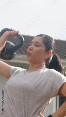 Vertical video: Lifting kettlebell, woman in leggings starting rep to overhead by house for fitness