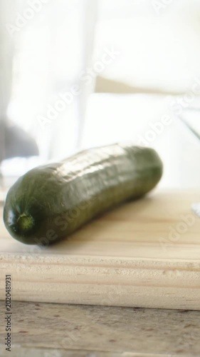 Vertical video: Pulling back camera revealing cucumber on cutting board by kitchen window, glass