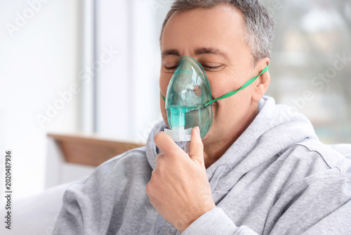Fotografie Middle aged man using nebulizer mask for respiratory treatment at home, inhalati